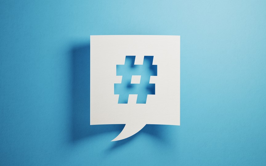 En hvid taleboble udklippet i midten så der fremstår et hashtag. Fremstår på en blå baggrund